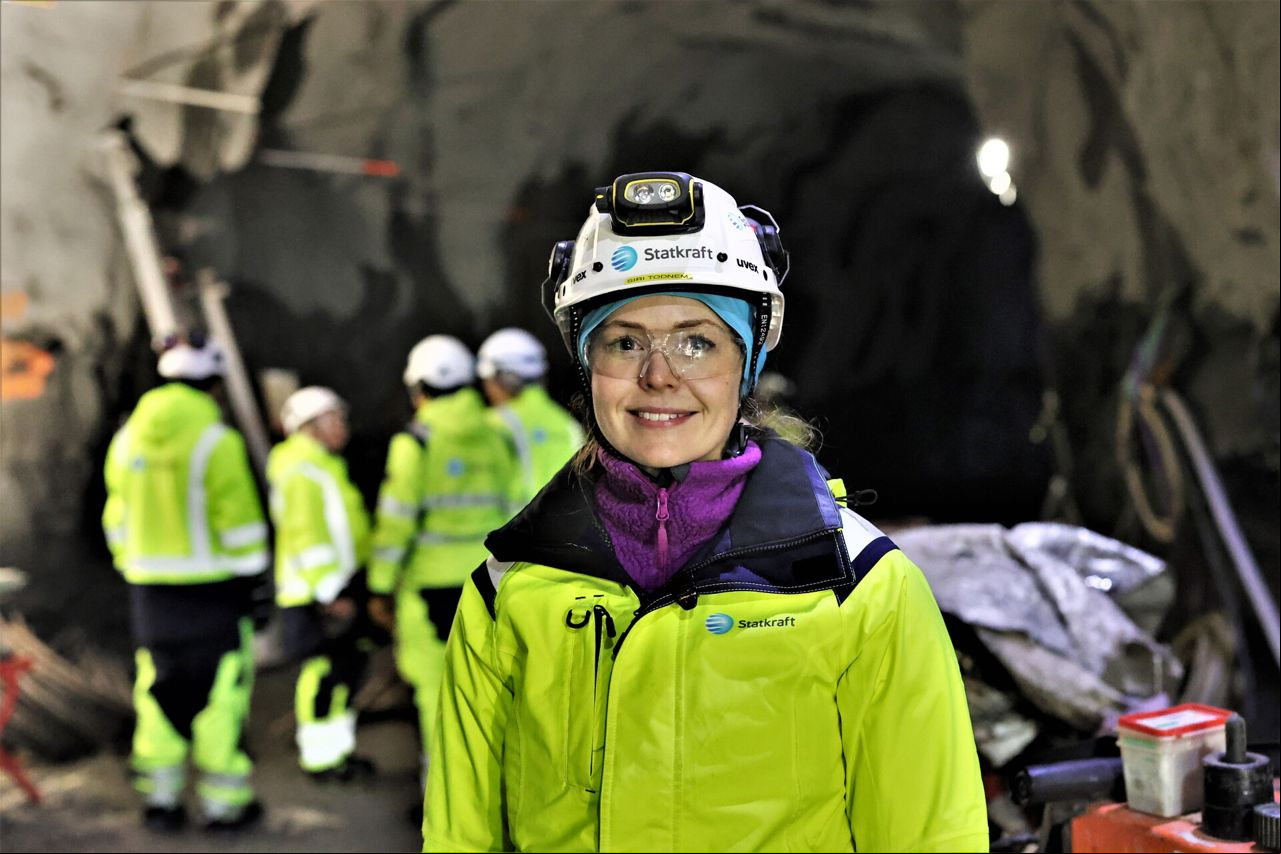 Uma mulher trajada com EPIs e uniforme da Statkraft. Em segundo plano, um grupo de pessoas.